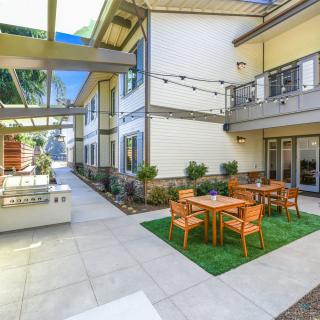 A modern courtyard featuring tables and chairs, enhanced by string lights and landscaping.