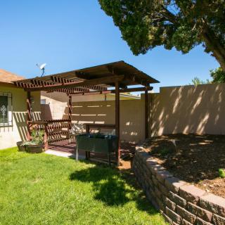 A sunny backyard with a pergola and outdoor seating area on a neatly maintained lawn.