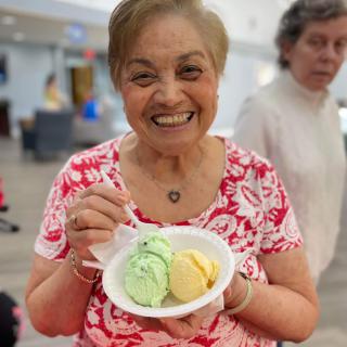 A woman happily holding a bowl of colorful ice cream indoors.