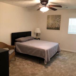 A simple bedroom with a bed, lamp, chair, and ceiling fan.