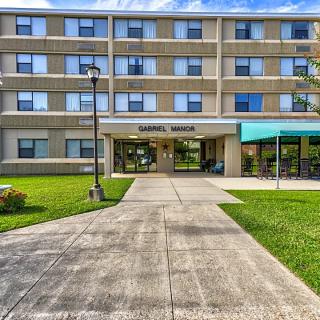 A multi-story building with a landscaped entrance and a concrete pathway leading to the main door.
