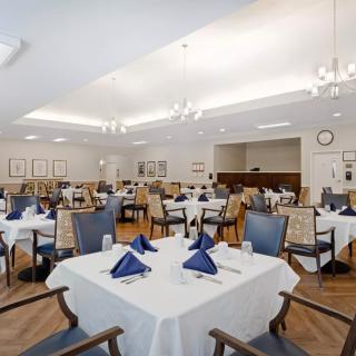 An elegantly set dining room with neatly arranged tables and chairs, featuring blue napkins and soft lighting.