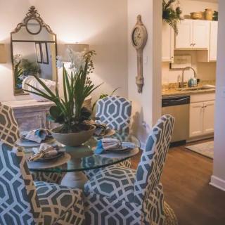 A stylish dining area with a glass round table and patterned chairs, adjacent to a kitchen.