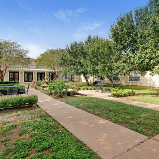 A peaceful garden with a pathway surrounded by trees and a building in the background.
