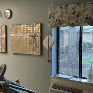 A cozy room featuring modern art pieces, a window with floral curtains, and a clock on the wall.