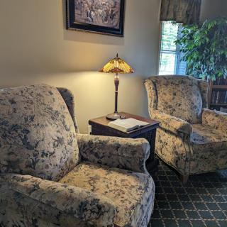 A cozy living room setting with floral patterned chairs, a lamp, and a touch of greenery.