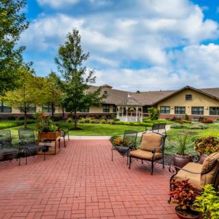 A spacious patio area with outdoor furniture, surrounded by well-maintained gardens and a large building in the background.