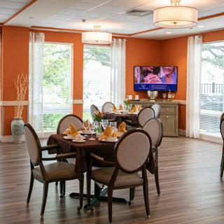 A cozy dining area with neatly arranged tables, an orange accent wall, and a television.