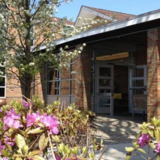 Entrance of a brick building adorned with blooming flowers and trees on a sunny day.