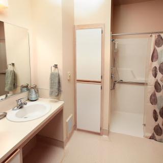 A well-lit bathroom featuring a shower, sink, mirror, and storage cabinets.