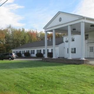 A white building with columns, surrounded by green grass and trees.
