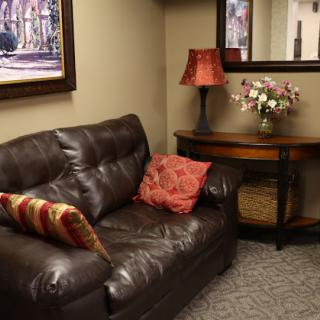 A cozy living room setup featuring a brown leather sofa, decorative pillows, a stylish lamp, and a mirror reflecting fresh flowers.