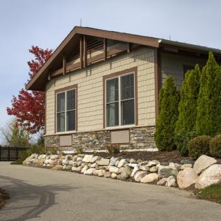 A modern house with stone siding, surrounded by lush greenery and a clear sky.