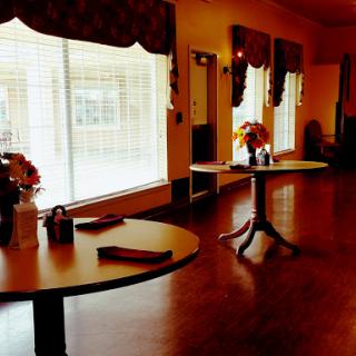 A warm and inviting interior space featuring tables adorned with flowers, natural light streaming through large windows.