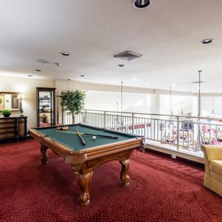 A spacious game room with a pool table and cozy seating area on red carpet flooring.