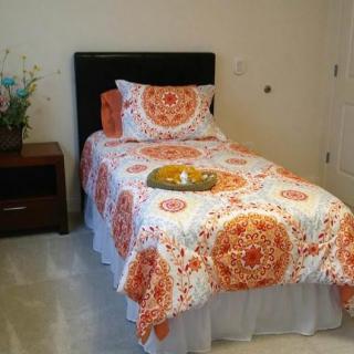 A neatly made single bed with a colorful bedspread and decorative pillow, accompanied by a wooden nightstand and a flower arrangement.