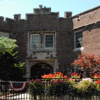 A brick building with a decorative entrance surrounded by vibrant flowers and greenery.