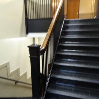 A view of an interior staircase with metal railings and a wooden handrail.