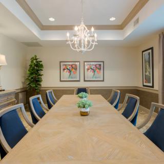 A well-lit conference room featuring a large meeting table surrounded by chairs, with a chandelier overhead and decorative artwork on the walls.