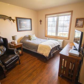 A cozy bedroom featuring a comfortable bed, a chair, and a television, illuminated by natural light from the window.