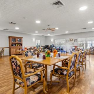 A bright and spacious dining room with neatly arranged tables and chairs, featuring a wooden floor and decorative elements.