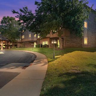 A well-lit building at dusk with a pathway and surrounding trees.