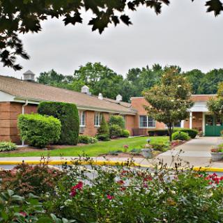 A tranquil scene featuring a well-maintained residential building surrounded by lush landscaping and blooming flowers on a cloudy day.