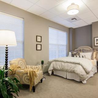 A cozy bedroom with neutral tones, featuring a comfortable bed, an upholstered chair, and a floor lamp.