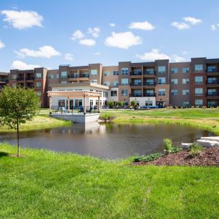 A modern apartment complex with a scenic pond and lush greenery.