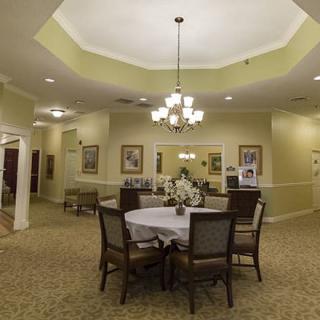 A well-lit dining area with a central table surrounded by chairs, adorned with floral decorations and a chandelier overhead.