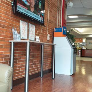 A view of a waiting area featuring a television displaying news, alongside informational materials on a table within a brick-walled interior.