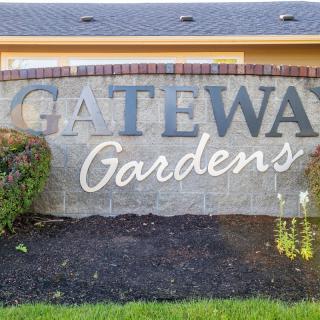 A stone sign for Gateway Gardens with bushes in front.