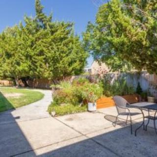 A sunny backyard featuring a patio with seating and lush greenery.