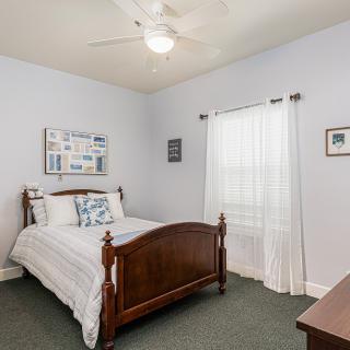 A cozy bedroom with a wooden bed, white bedding, and a ceiling fan.