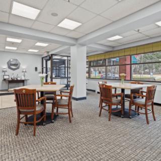 A bright and spacious cafeteria with wooden tables and chairs, featuring large windows.