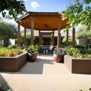 A beautifully landscaped patio with a wooden gazebo and outdoor seating surrounded by lush plants.