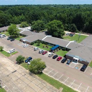 Aerial view of a commercial complex surrounded by trees and featuring an organized parking lot.