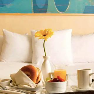 A cozy breakfast in bed setup with a bagel, fruit, juice, coffee, and a flower.