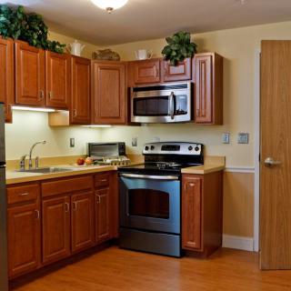 A modern kitchen with wooden cabinets, stainless steel appliances, and a wooden floor.
