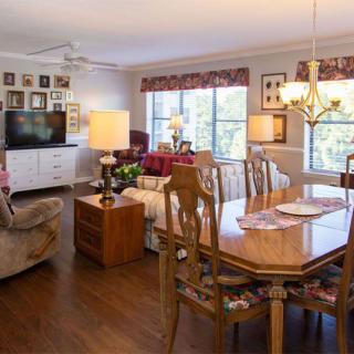 A cozy living and dining area with wooden flooring, featuring a dining table, comfortable seating, a television, and large windows allowing natural light.