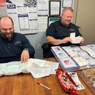 Two men enjoying gifts and snacks in an office setting.