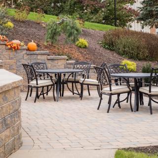 An outdoor patio with metal tables and chairs, surrounded by garden landscaping and decorated with pumpkins for autumn.