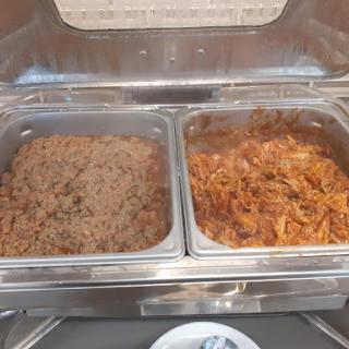 A view of two trays at a buffet: one filled with seasoned rice and the other with a savory meat dish.