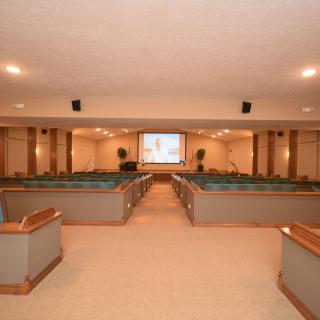 A church interior with rows of pews and a central aisle leading to a baptismal font and projector screen.