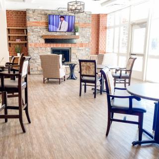 A cozy lounge area with chairs and tables, featuring a fireplace and a television mounted above.