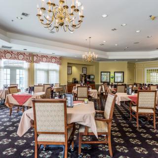 A spacious dining room with neatly arranged tables and chairs under elegant chandeliers.