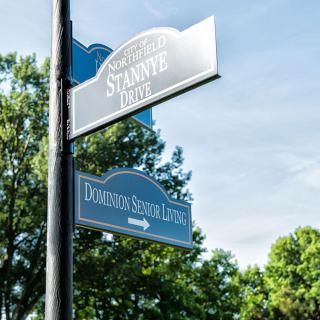 Street signs at an intersection with trees and clear sky in the background.