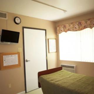A hospital room with a single bed, wall-mounted television, and a window allowing natural light.
