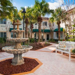 A tranquil courtyard featuring a decorative fountain surrounded by palm trees and benches.
