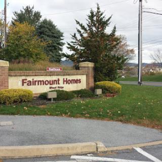 Entrance sign for Fairmount Homes surrounded by greenery and a cloudy sky.